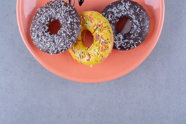 An orange plate of delicious chocolate doughnuts with sprinkles. 