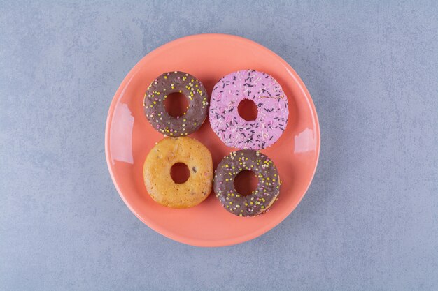 An orange plate of delicious chocolate doughnuts with sprinkles.