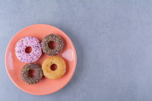 An orange plate of delicious chocolate doughnuts with sprinkles.