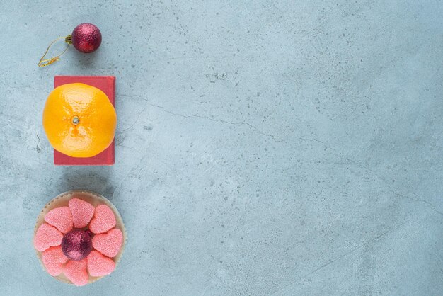 Orange on a red box next to a small platter of marmelades around a decorative ball on marble.