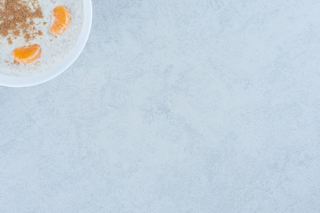 Foto gratuita fette d'arancia e cannella in polvere sopra il porridge in una ciotola sul marmo.