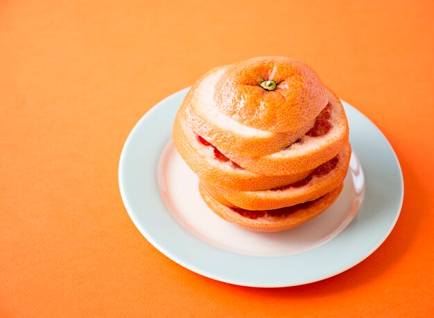 An orange slices stacked over another on white plate against colored background