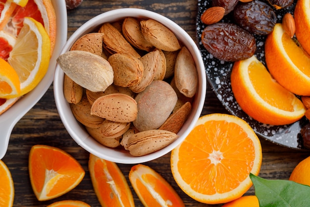 Orange slices with dates, almonds, grapefruit slices and leaf in plates on wooden table, flat lay.