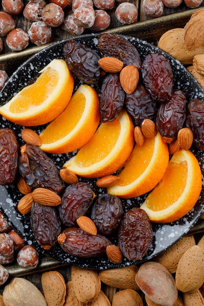 Free photo orange slices with dates, almonds and nuts in a plate on copper tray