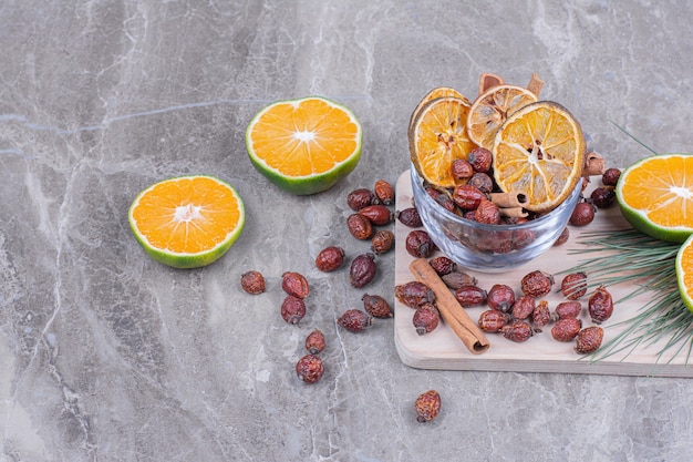 Orange slices with dry hips and cinnamon sticks on a wooden platter