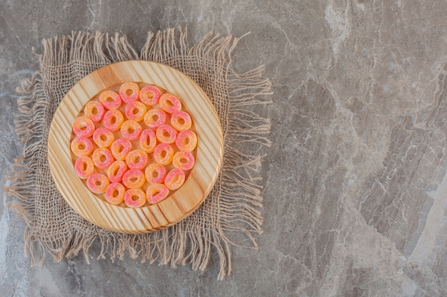 Orange sweet candies in ring shape on wooden plate over sack.