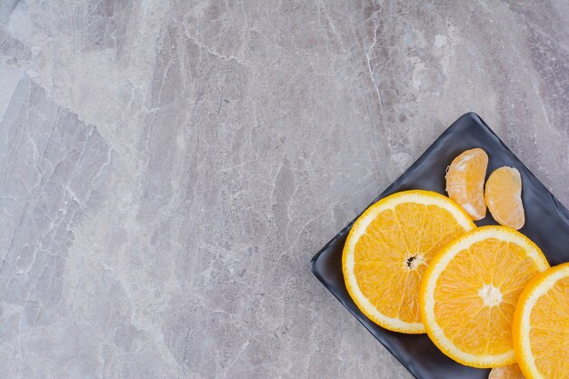 Orange and tangerine slices on black plate.