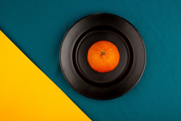 Orange tangerine a top view of fresh ripe mellow juicy whole inside black plate on a yellow-blue floor