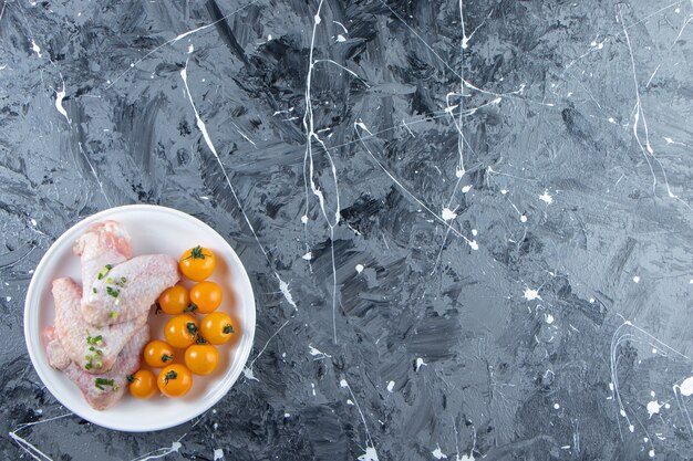 Orange tomatoes and chicken wings on a plate , on the marble background. 