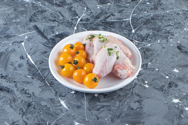 대리석 표면에 접시에 오렌지 토마토와 닭 날개.