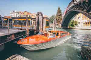 Foto gratuita barca arancio del canale navigabile su un fiume sotto un ponte vicino alle costruzioni a venezia, italia