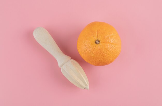 Orange and wooden reamer on pink table. 