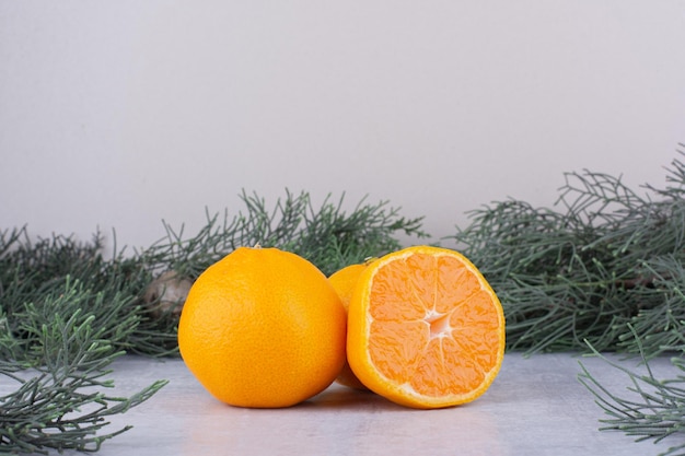 Oranges bundled next to pine branches on white surface