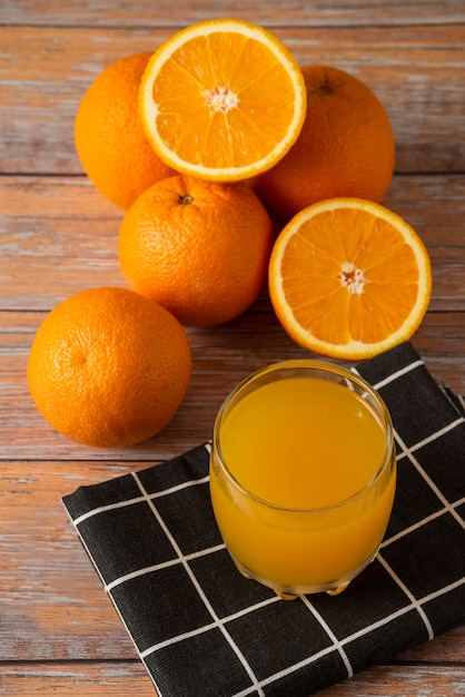 Oranges and a glass of juice on a black kitchen towel, top view