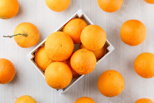 Oranges in a wooden box on a white wooden surface. flat lay.
