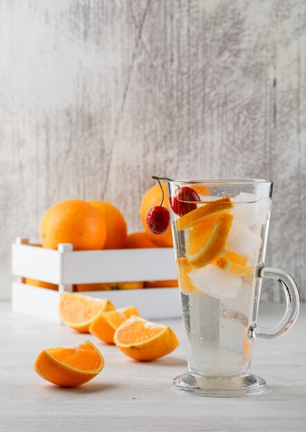 Oranges in a wooden box with fruit infused water side view on white surface