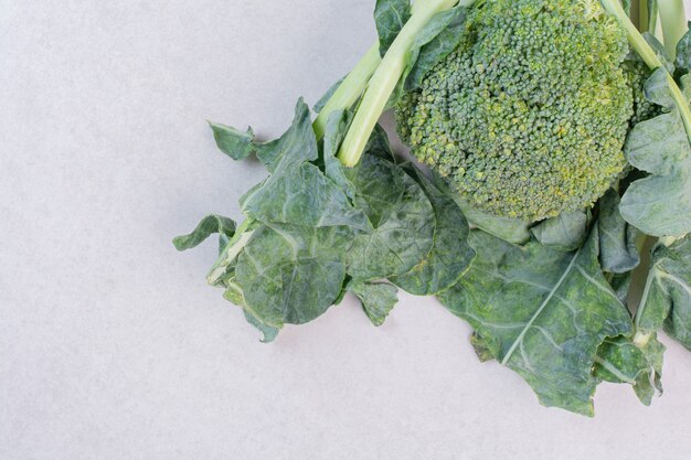 Organic broccoli with leaves on white surface
