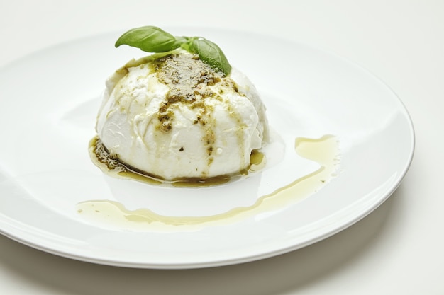 Organic buffalo mozzarella cheese topped with pesto sause and basil herb leaves on top.