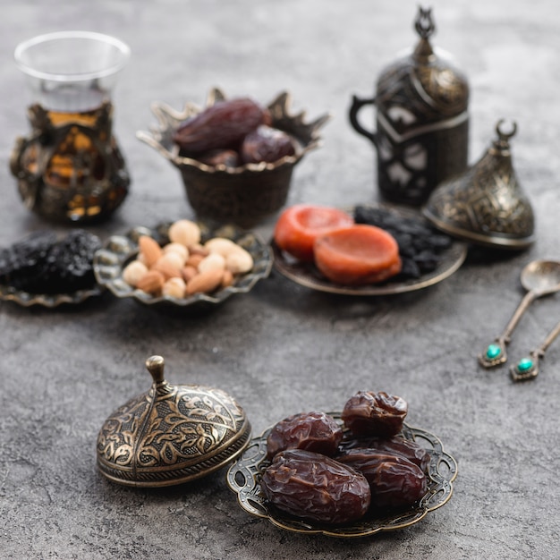 An organic dates on bronze plate in front of dried fruits; tea and nuts on concrete surface