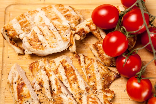 Foto gratuita cibo delizioso biologico. petto di pollo fresco alla griglia su tavola di legno accanto ai pomodori. cena e stile di vita sani