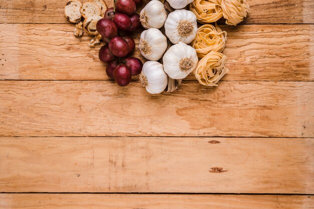Organic grapes; bunch of garlic bulbs with raw pasta and bread over textured wallpaper