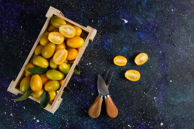 Foto gratuita kumquat organici in una scatola di legno sulla superficie blu