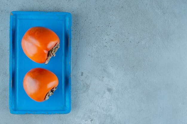 Organic persimmons on a blue wooden plate , on the marble background.