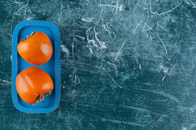 Organic persimmons on wooden tray , on the marble table. 