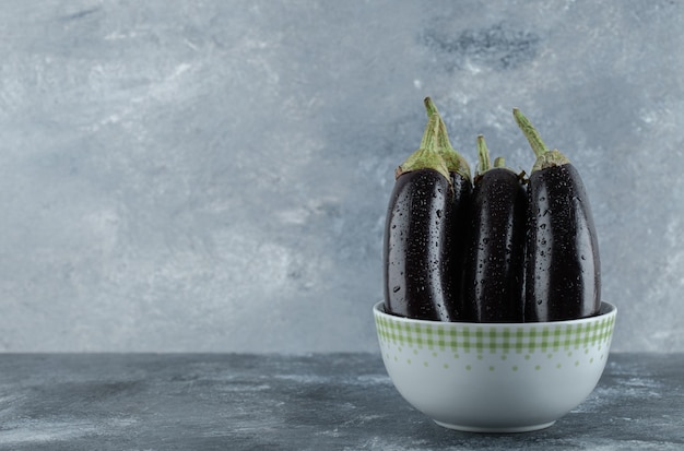 Organic raw eggplants in bowl on grey background.