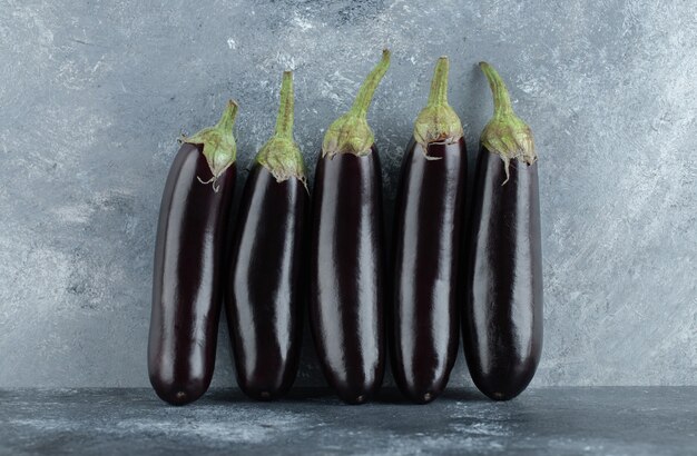 Organic ripe aubergine row on grey background.