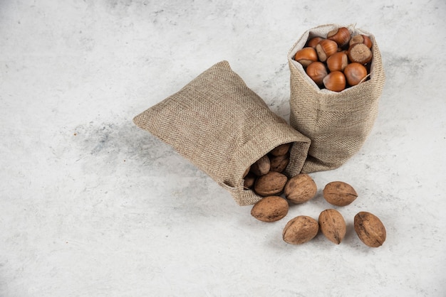 Free photo organic shelled hazelnuts and walnuts in sackcloth on marble table.