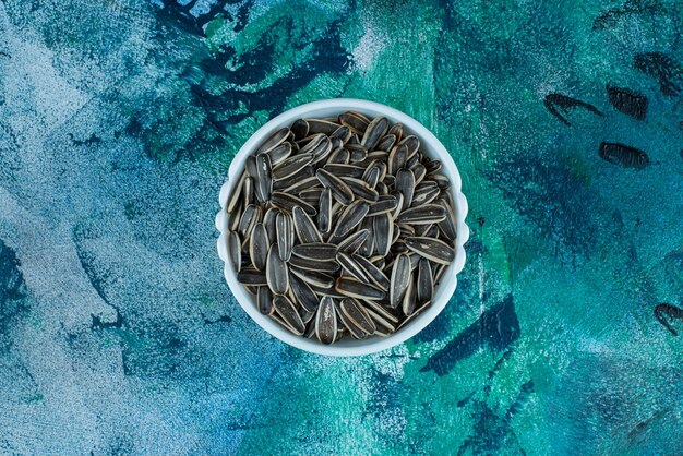 Organic sunflower seed in a bowl, on the blue table.