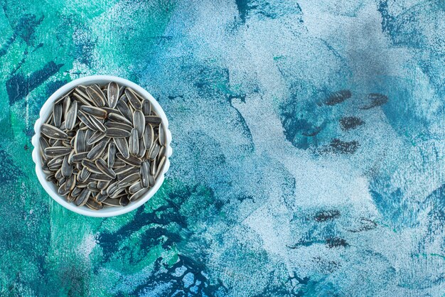 Organic sunflower seed in a bowl, on the blue table.