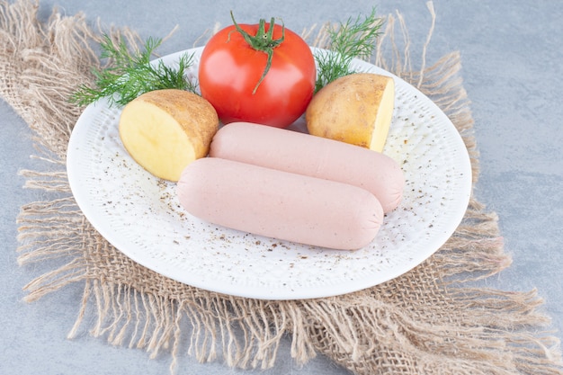 Organic vegetables and fresh sausage on white plate. 