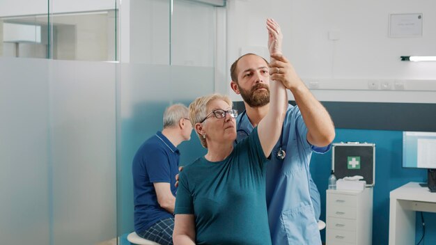 Orhopedic specialist doing arms stretch exercise with elder patient, helping with physical therapy. Male osteopath giving assistance to senior woman, recover from mechanical disorders.