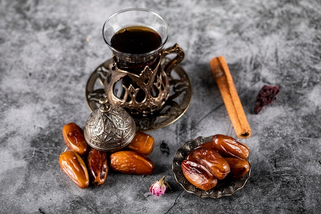 Oriental dates in an ethnic style saucer with a glass of tea and cinnamon sticks. 