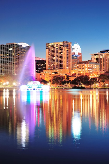 올랜도 시내 스카이라인은 밤에 도시 고층 빌딩, 분수, 맑은 하늘이 있는 에올라 호수(Lake Eola) 위로 파노라마로 펼쳐집니다.