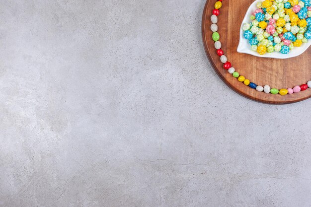 An ornate plate of candies surrounded by candies on wooden board on marble background. 