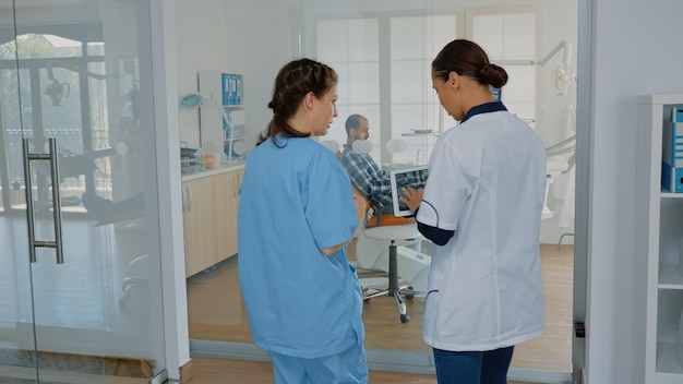 Orthodontic team discussing teethcare with x ray scan at dental clinic. Dentist wearing uniform starting patient consultation in cabinet using stomatological equipment and technology