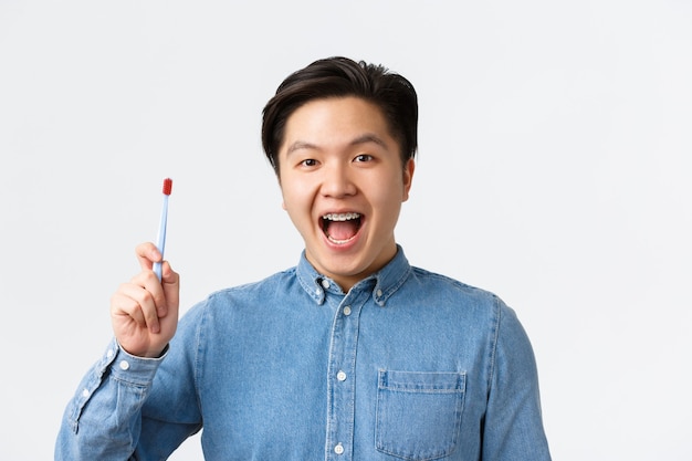 치열 교정, 치과 치료 및 위생 개념입니다. 웃고 있는 쾌활한 아시아 남성은 뜨거운 치아 교정기를 보여주고 칫솔을 들고 입을 벌리고 치약, 흰색 배경을 추천합니다.