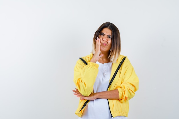 Ortrait of lady keeping hand on cheek in t-shirt, jacket and looking confused front view