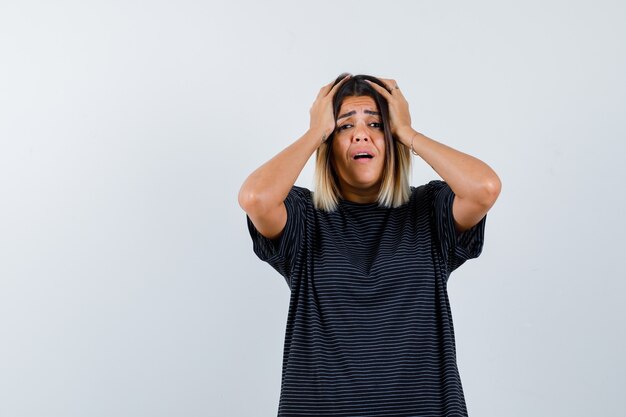 Ortrait of lady keeping hands on head in black t-shirt and looking wistful front view