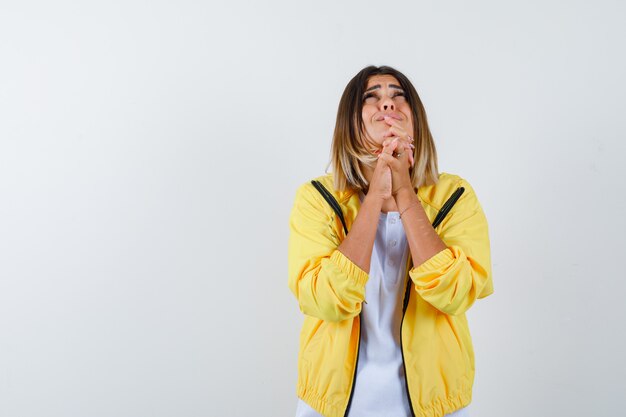 Ortrait of lady keeping hands in praying gesture in t-shirt, jacket and looking sorrowful front view
