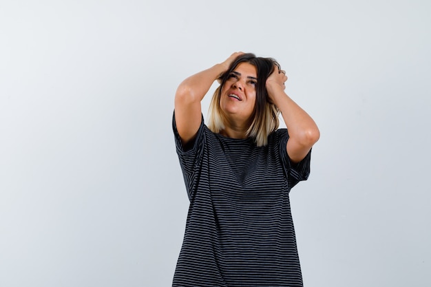 Free photo ortrait of young lady holding hands on head while looking up in polo dress and looking thoughtful front view