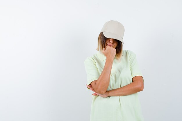 Tシャツ、キャップ、思慮深い正面図でポーズを考えて立っている若い女性のOrtrait