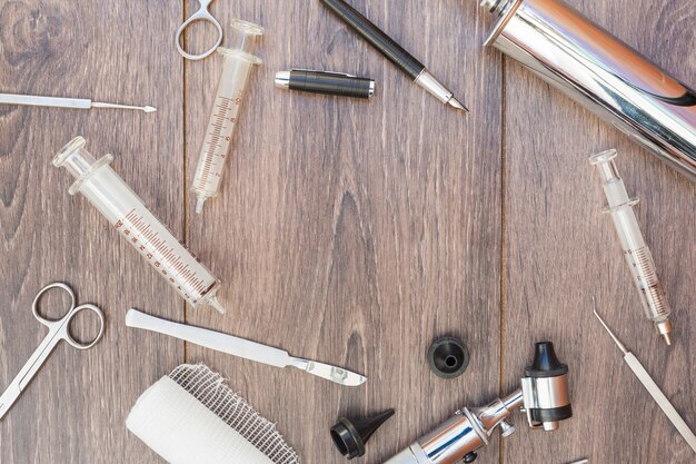 Otoscope; syringe; surgical instruments; roll gauze and black fountain pen on wooden desk