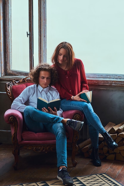 Free photo ouple of young students reading together and sitting on a chair.