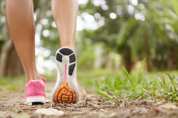 Outdoor activity and sports. Freeze action closeup of pink running shoes against green grass. Woman jogger exercising in park or forest, getting prepared for marathon.