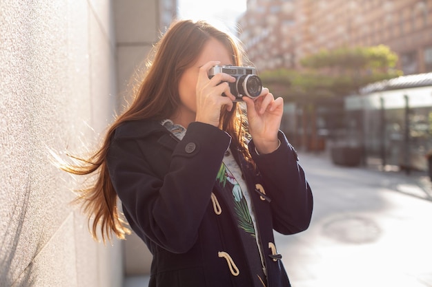 Outdoor autumn smiling lifestyle portrait of pretty young woman, having fun in the city with camera, travel photo of photographer. Making pictures in hipster style.