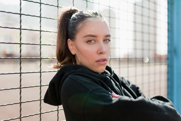 Outdoor close up portrait of brunette charming lady is posing at camera in sunlight in warn spring day on sport square